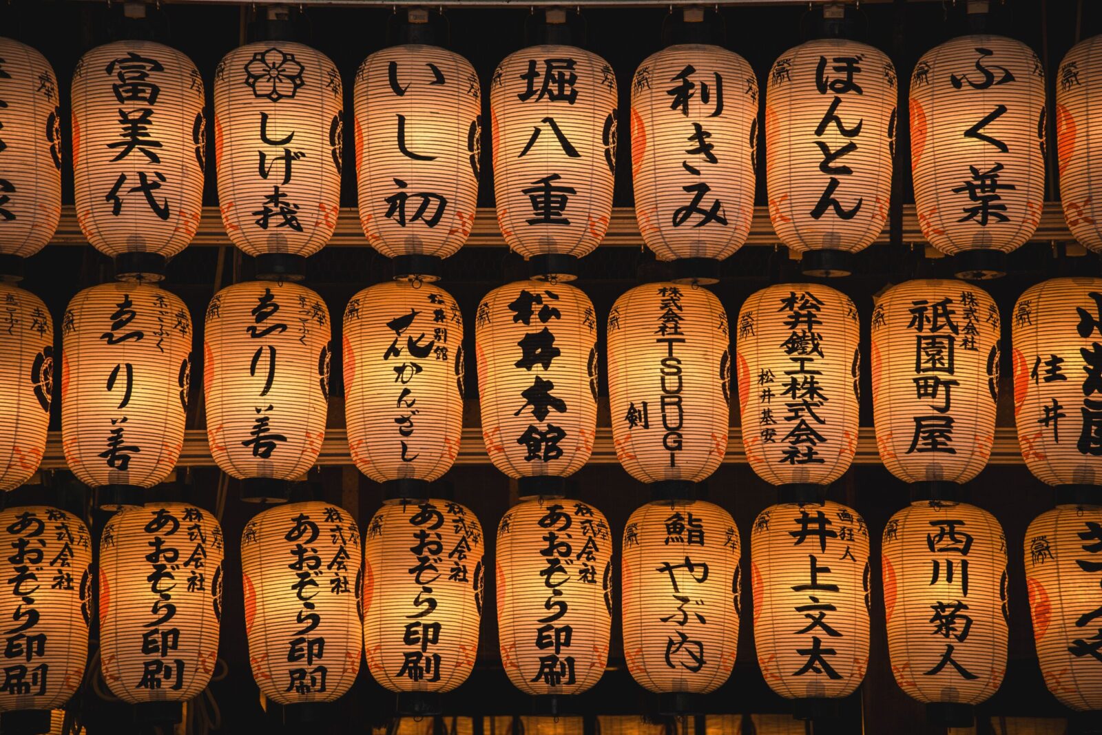 A display of glowing Japanese paper lanterns with kanji characters set against a dark background.